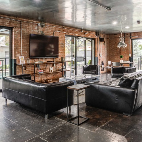 Clubhouse Lounge and lobby at our loft apartments for rent in Deep Ellum, featuring wood grain floor paneling and exposed brick.